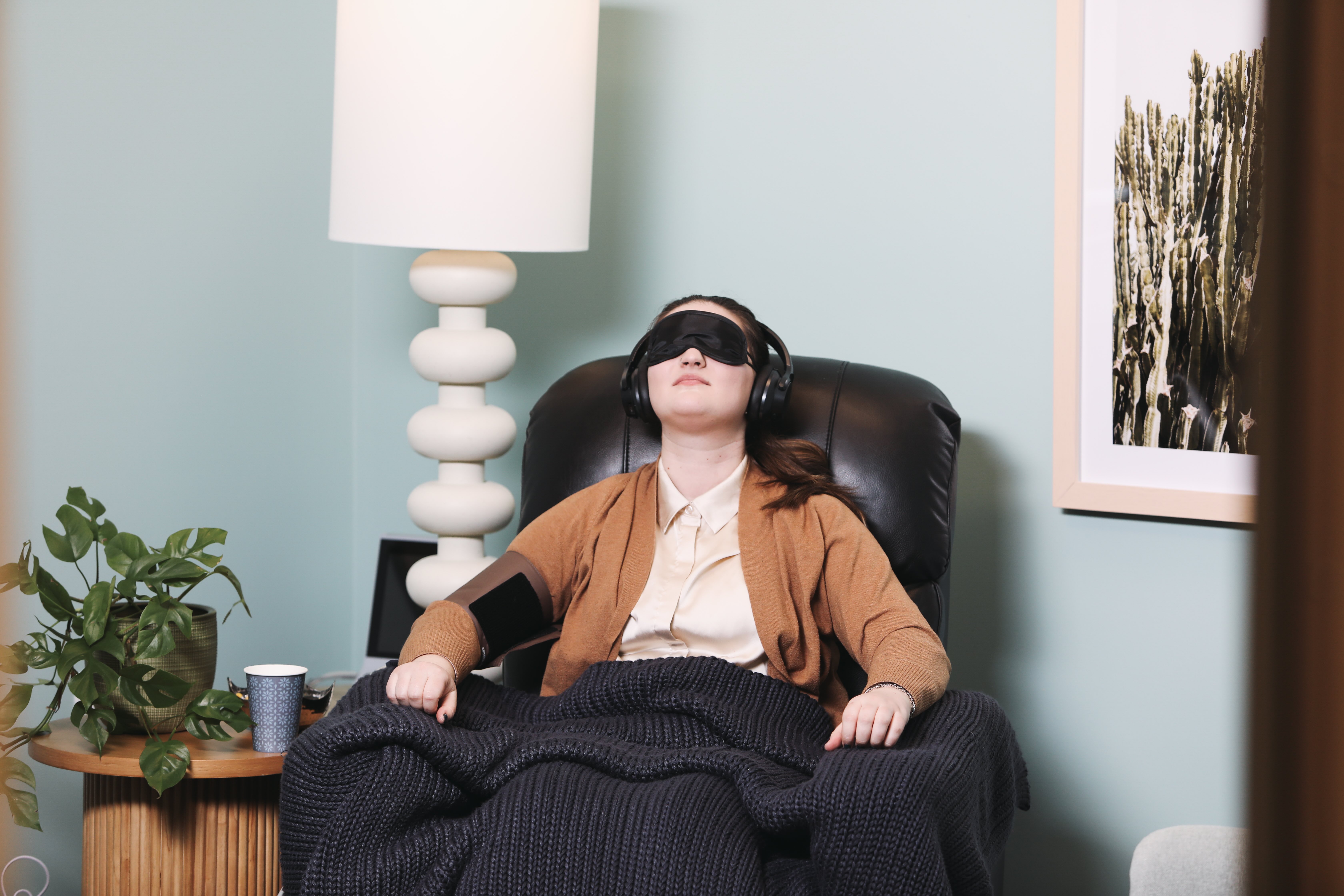 A woman reclining with an eye mask and headphones under a blanket in a calm, softly lit room