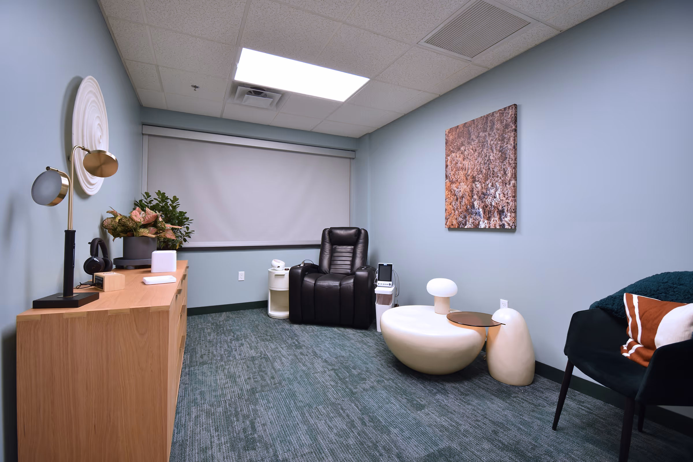 A calm Lumin Health treatment room with a black recliner, soft side tables, and warm lighting