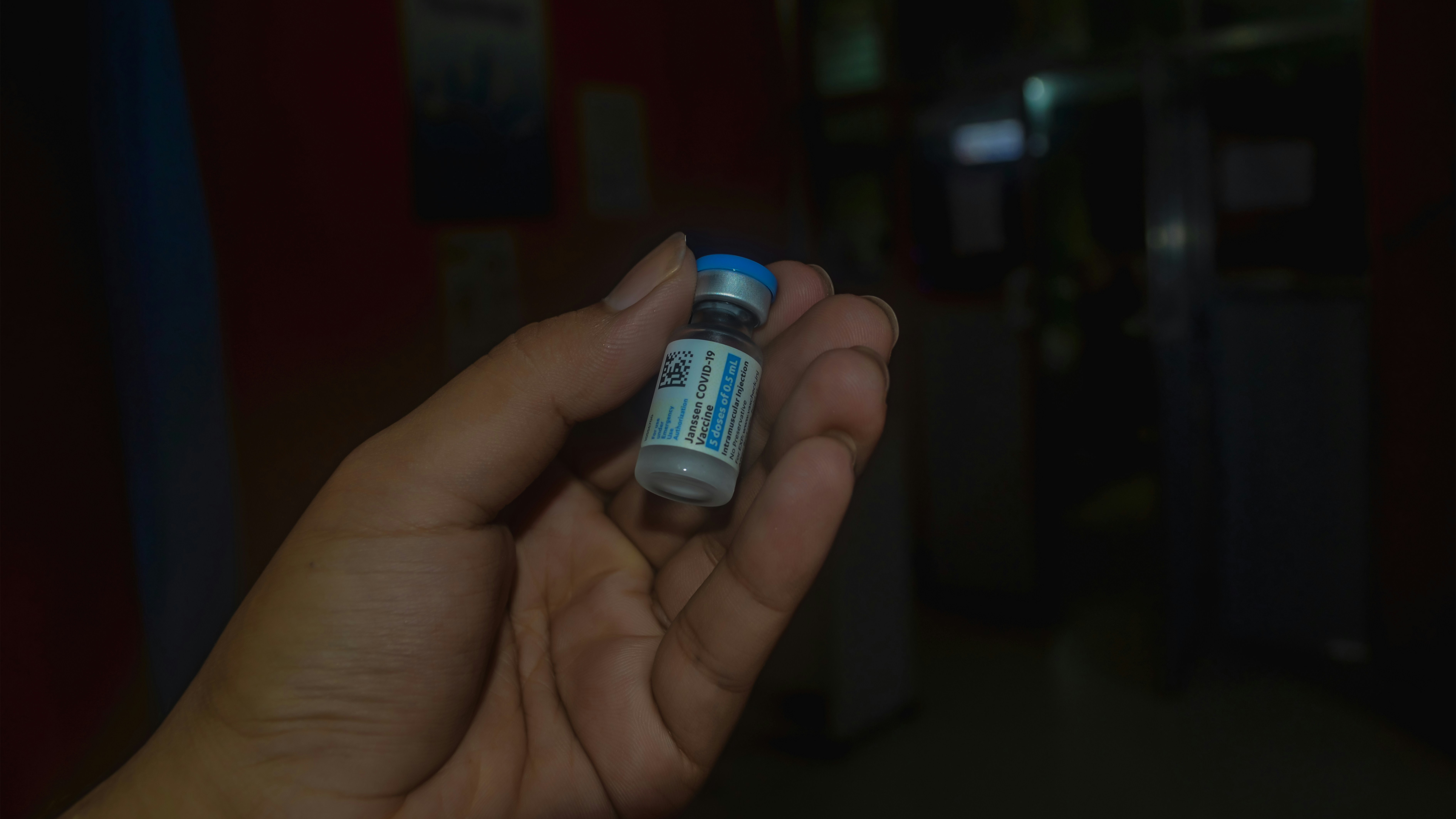 A hand holding a small labeled medication vial with a blue cap in dim light