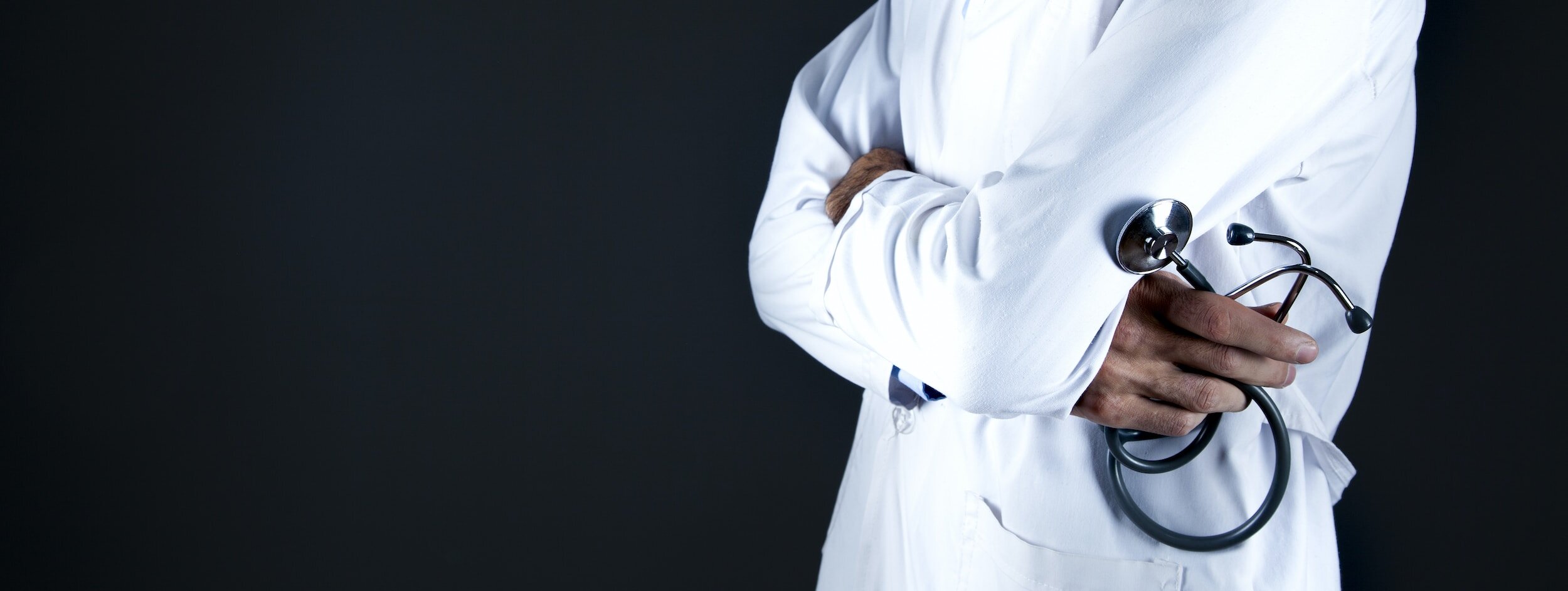 A doctor in a white coat with arms crossed holding a stethoscope against a dark background