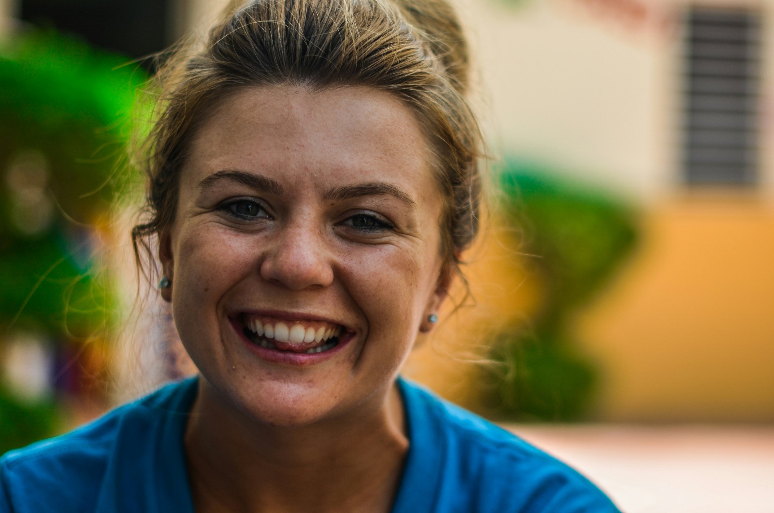 A smiling young woman with blonde hair outdoors in a blue shirt