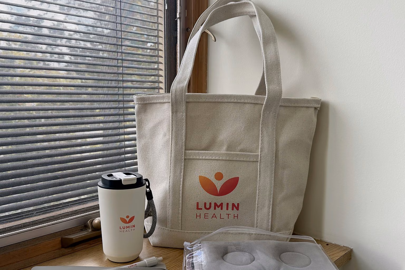 A Lumin Health canvas tote, travel cup, eye mask, notebook and pen on a windowsill