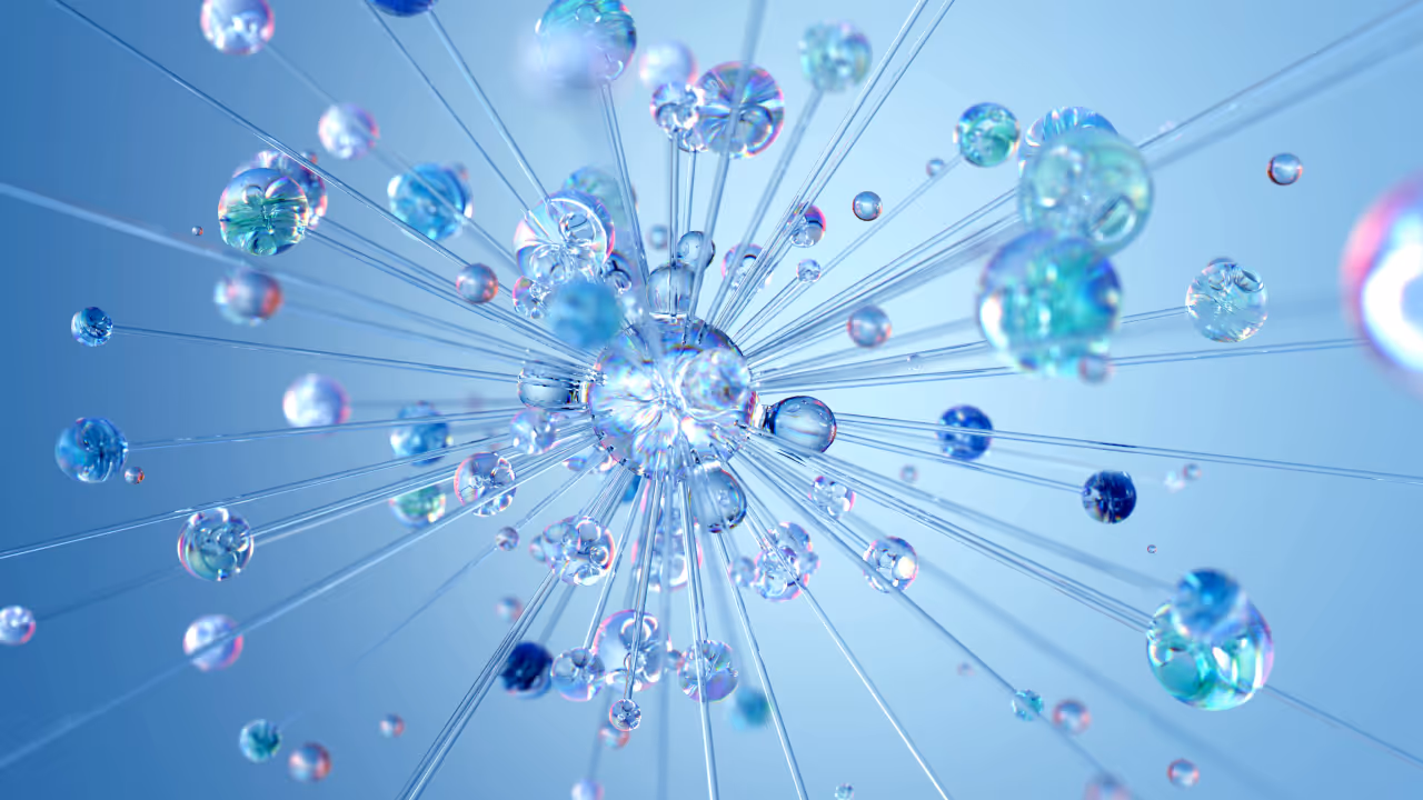 Abstract 3D rendering of a crystalline explosion or starburst pattern. Multiple translucent spheres in blue and turquoise tones appear to radiate outward from a central point along straight lines, creating a dynamic, symmetrical structure against a light blue background. The spheres have a glass-like quality with rainbow reflections and varying sizes.