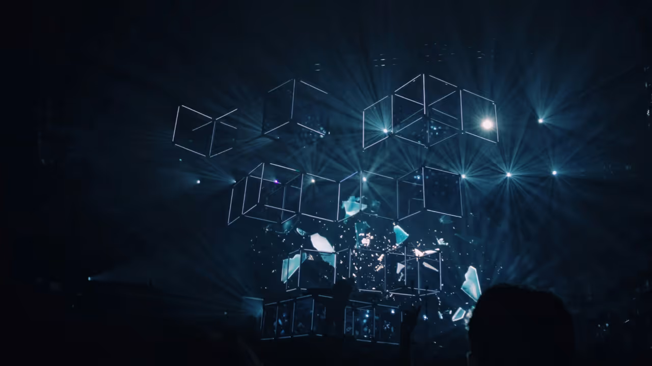 Abstract digital art showing illuminated 3D wireframe cubes floating in a dark space with bright blue light beams and scattered glowing fragments, symbolising data processing and technology.