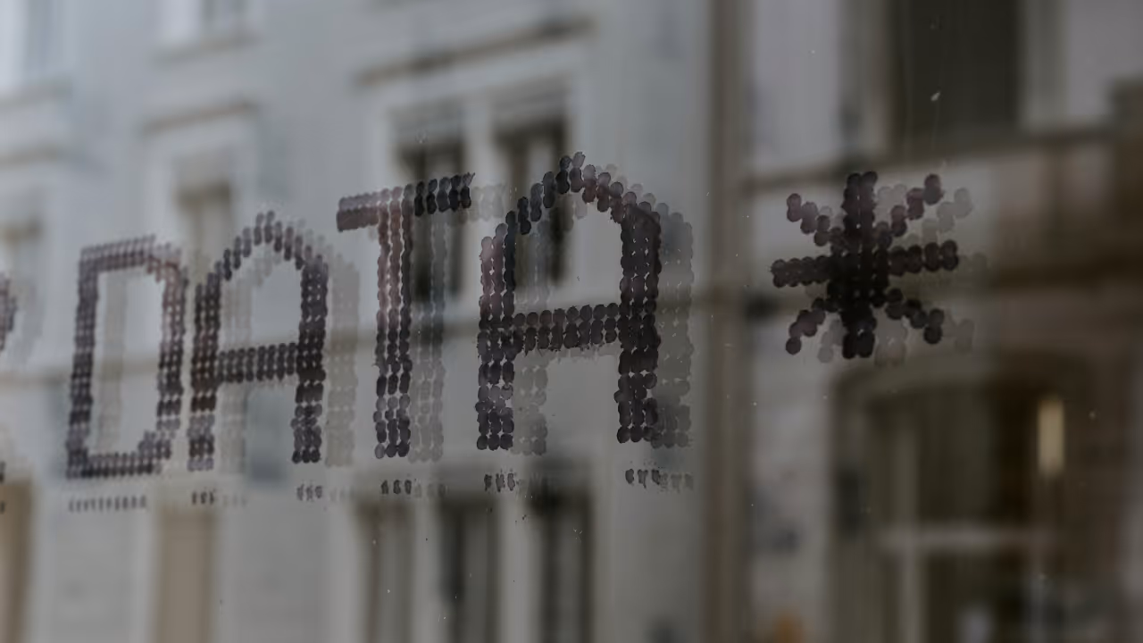 Close-up of the word ‘DATA’ and an asterisk symbol displayed on a glass window, with blurred buildings visible in the background.