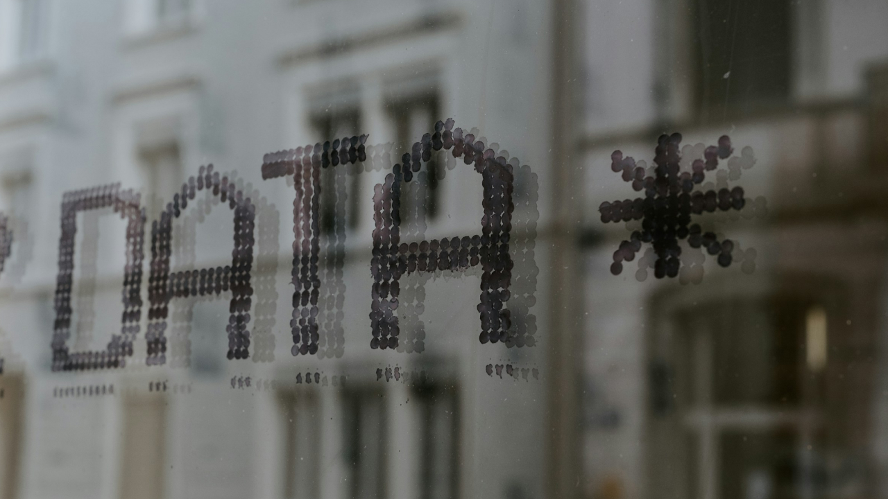Close-up of the word ‘DATA’ and an asterisk symbol displayed on a glass window, with blurred buildings visible in the background.