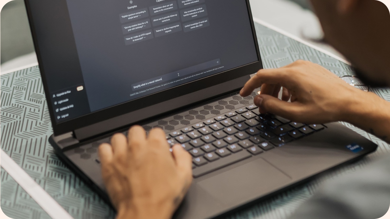 Person typing on a laptop displaying a ChatGPT interface, with both hands on the keyboard in a dimly lit setting.