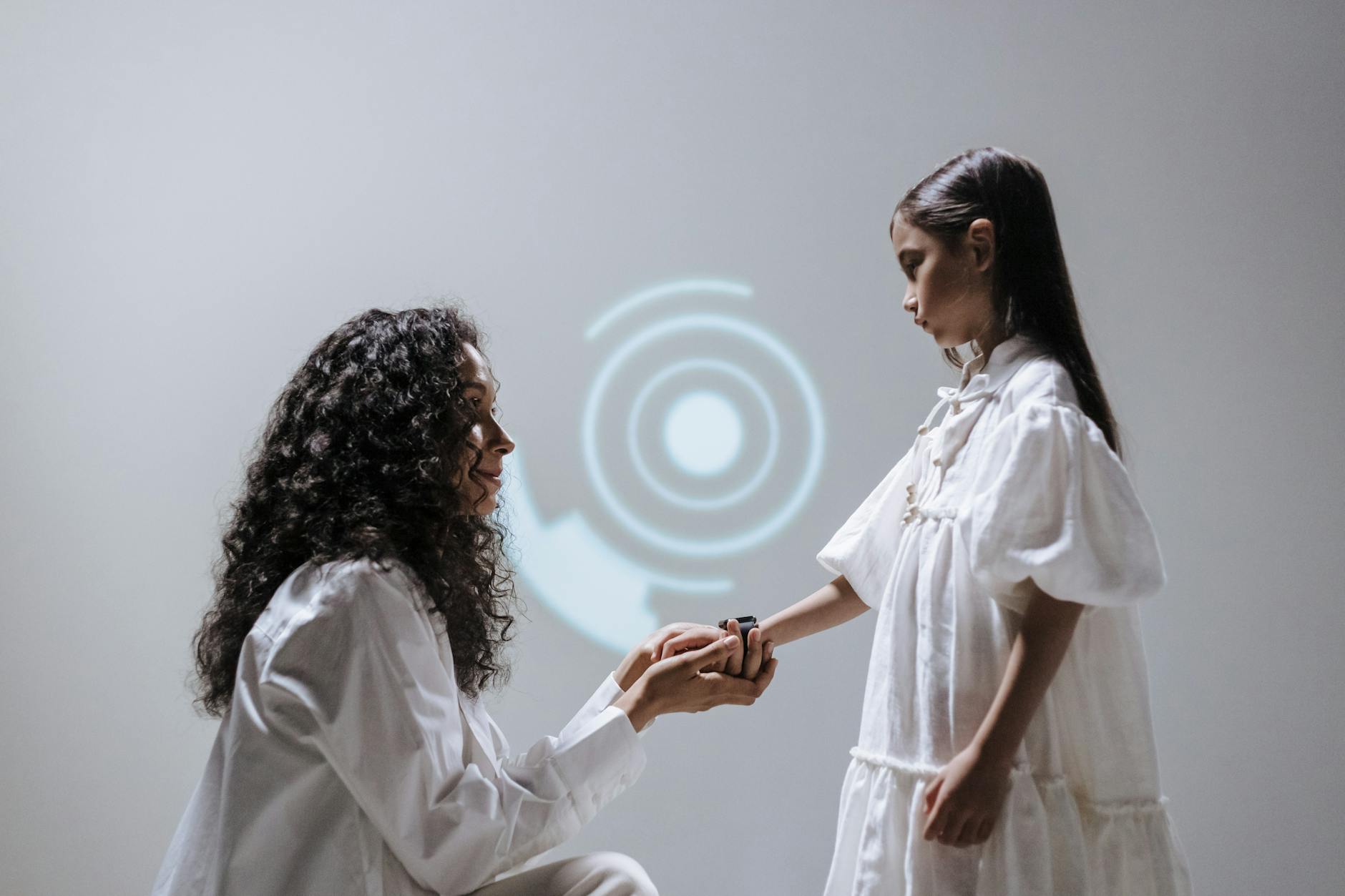 A mother kneeling and holding her daughter's hand, showcasing a smartwatch in a futuristic setting.