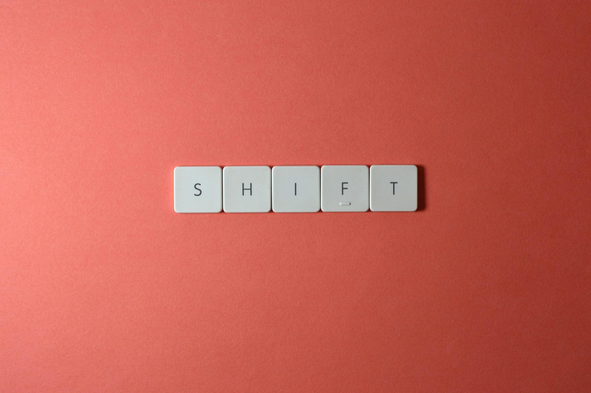 Close-up of keyboard keys spelling 'shift' on a plain red surface.