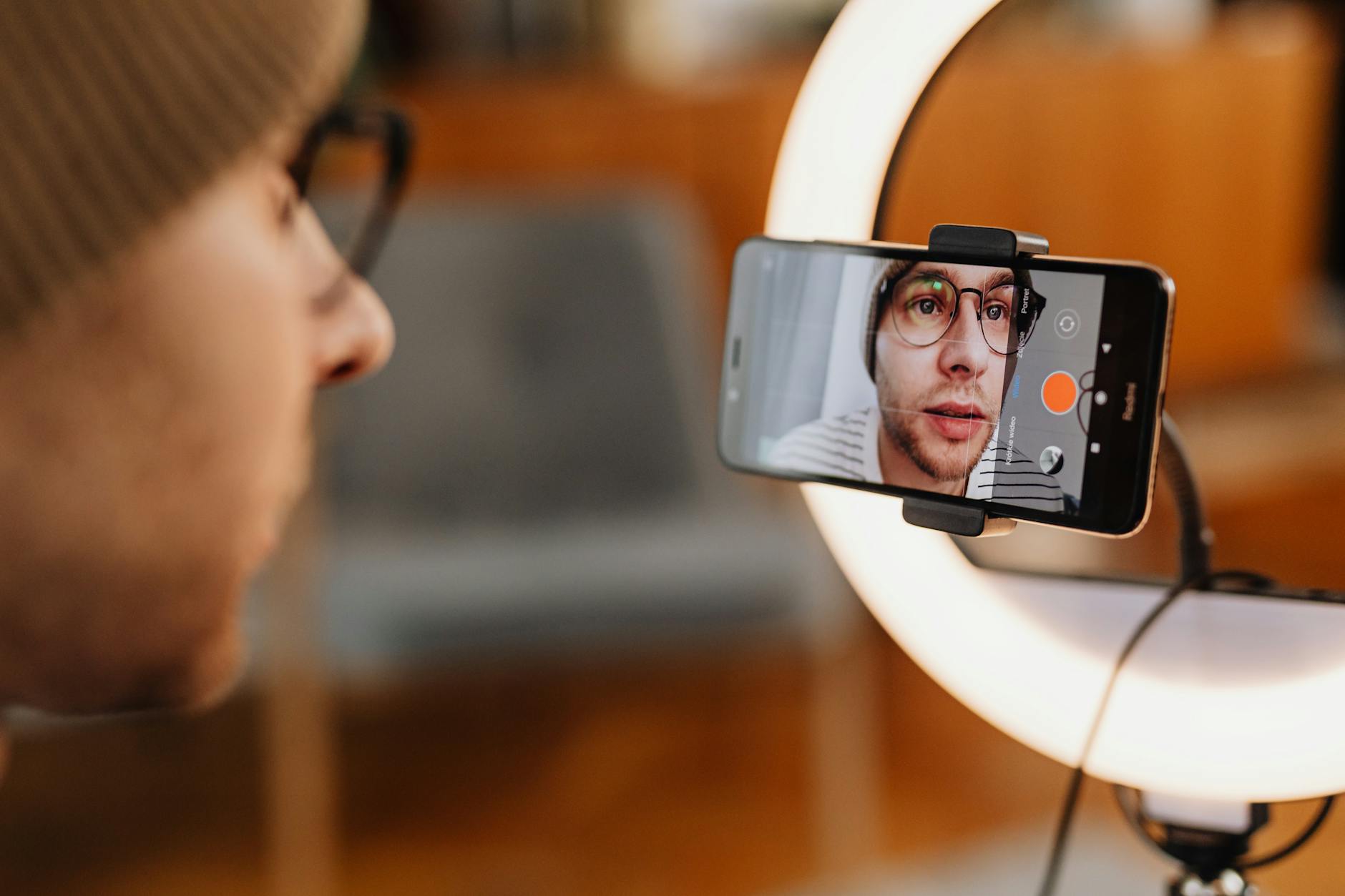 Close-up of a man recording a video with a smartphone and ring light indoors.