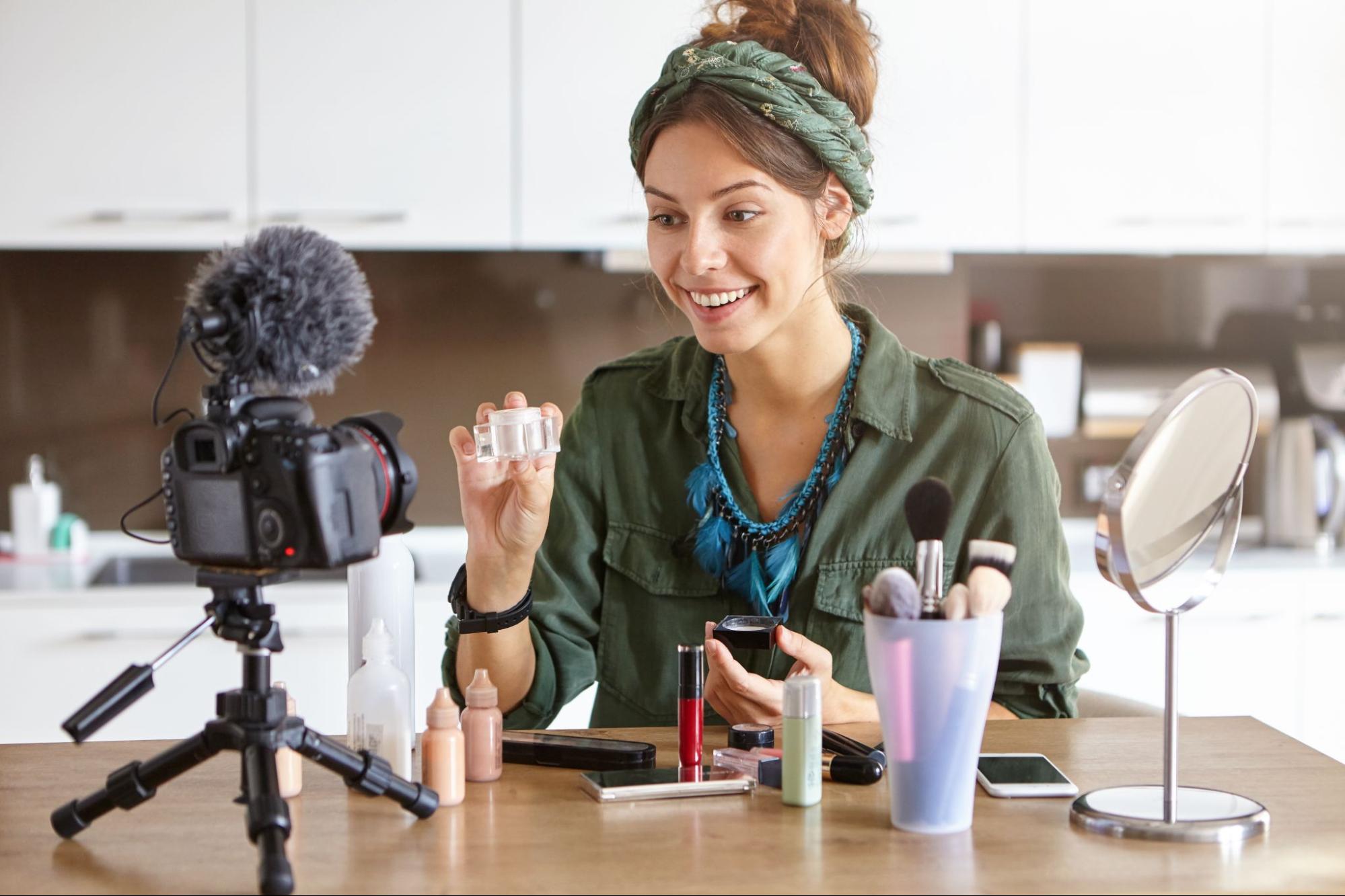 A female content creator filming a makeup tutorial video with all her makeup and a camera on the table.