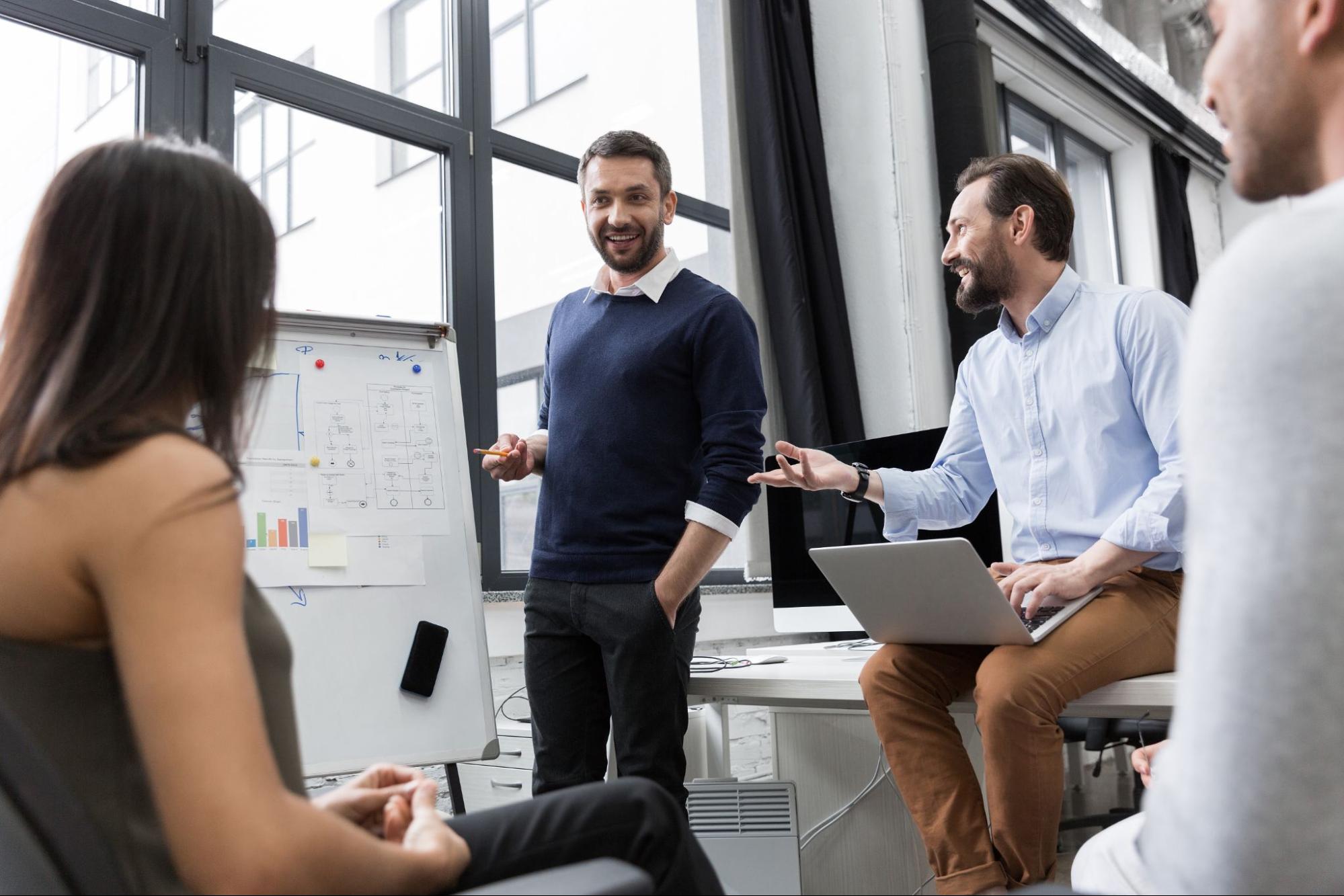 A man explaining a concept on a white board to a room full of people.