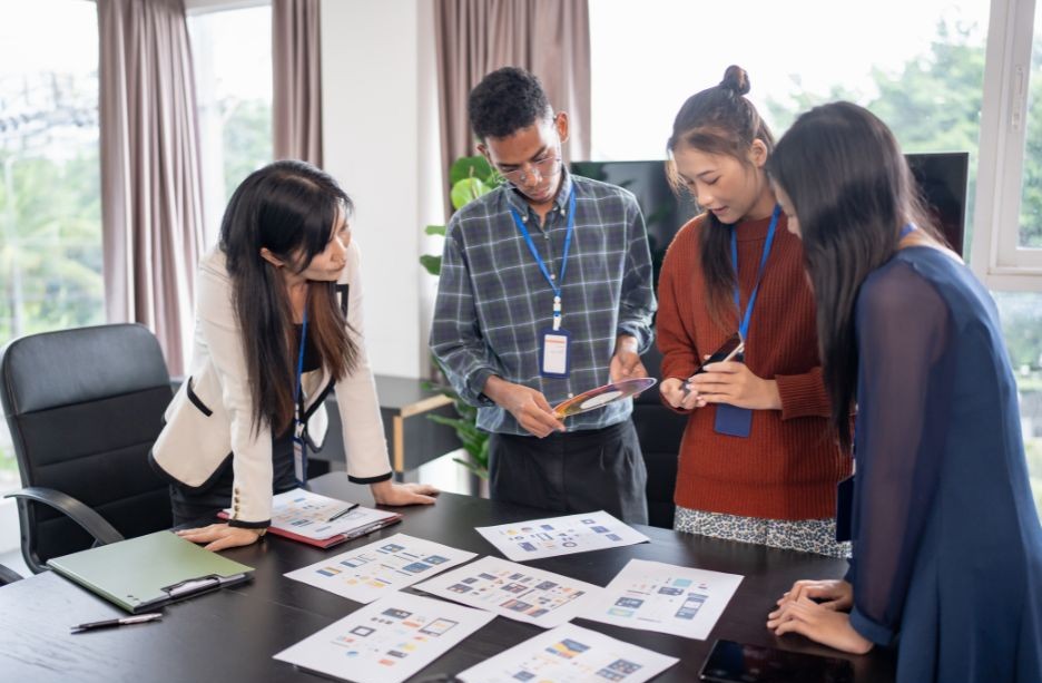 Employees gathered around a table filled with paper, deep in a discussion.