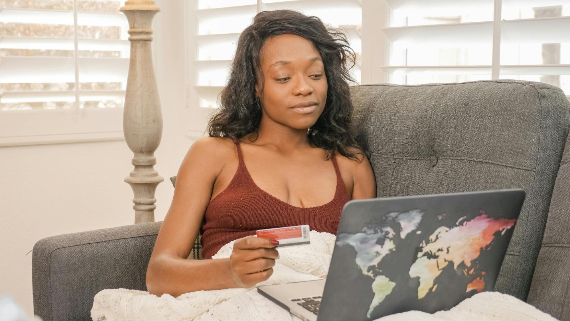 A woman sitting with her credit card in hand with a laptop on her lap.