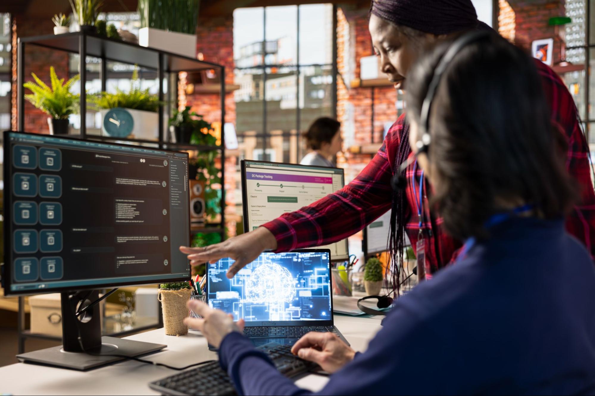 Colleagues discussing an automation software on a desktop screen with a laptop also open on the table.