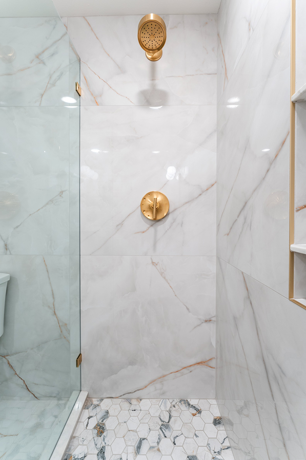 Full tile shower wall with brass fixture and mosaic flooring in a remodeled bathroom in Bothell