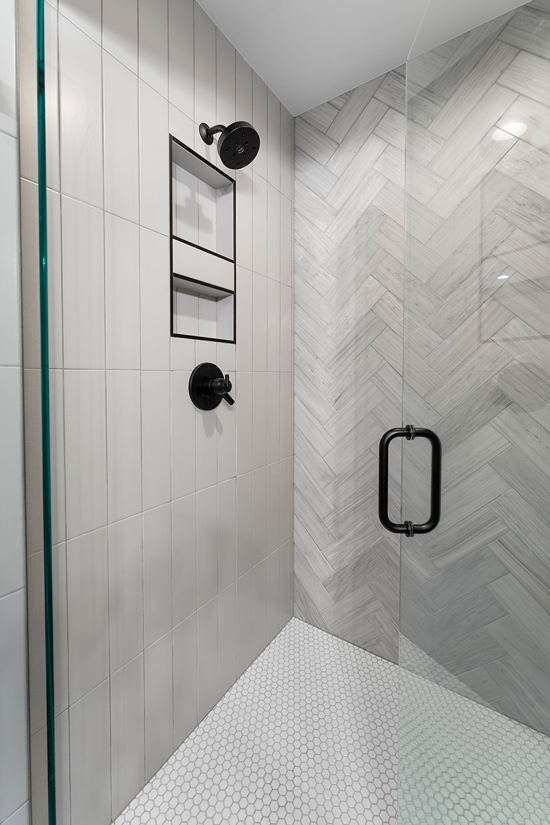 Walk-in shower in Bothell with a recessed tile niche between the valve and showerhead, tiled walls, hexagon mosaic floor tile, and a glass door