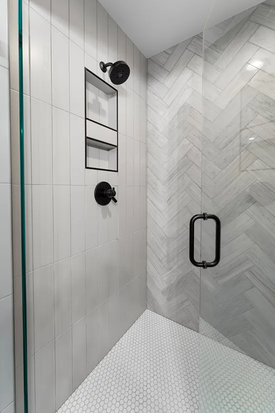 Walk-in shower in Bothell with a recessed tile niche between the valve and showerhead, tiled walls, hexagon mosaic floor tile, and a glass door