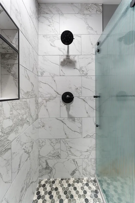 Walk-in shower with fluted glass enclosure and hexagon tile flooring