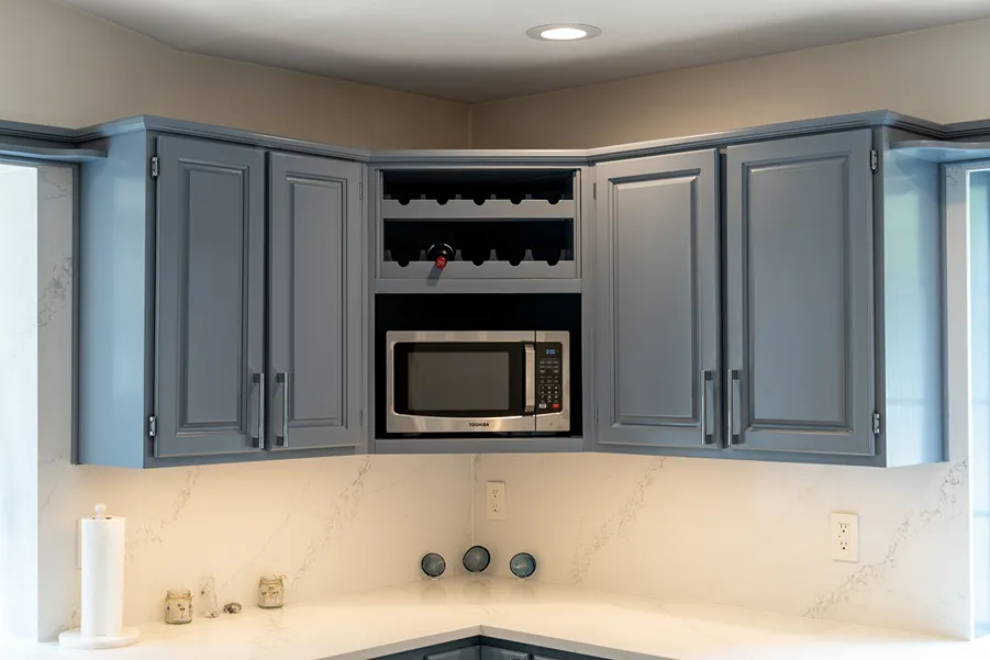 Slate blue painted upper kitchen cabinets and built-in wine rack above a white marble-look quartz countertop.
