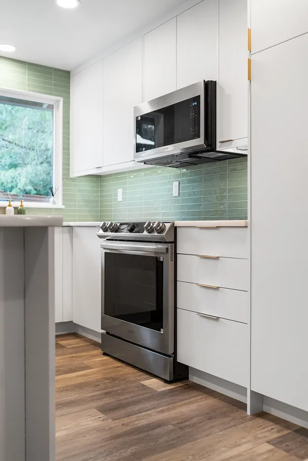 White painted kitchen cabinets and drawers with brass pulls framing a stainless steel slide-in range and microwave