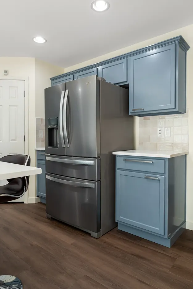 Fully painted slate blue kitchen cabinets surrounding a stainless steel refrigerator