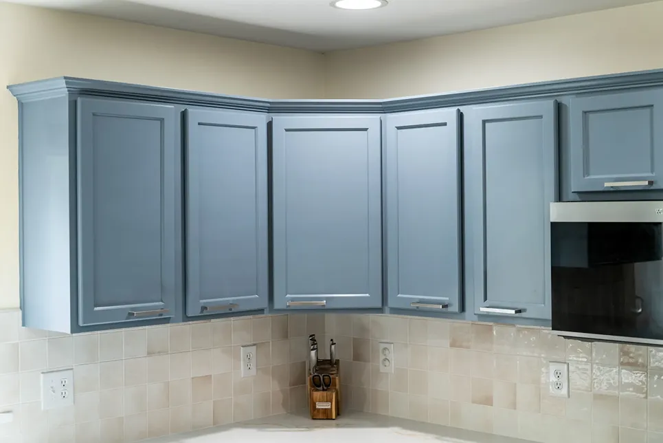 Slate blue painted upper wall cabinets with silver horizontal pulls installed above an off-white square tile backsplash.