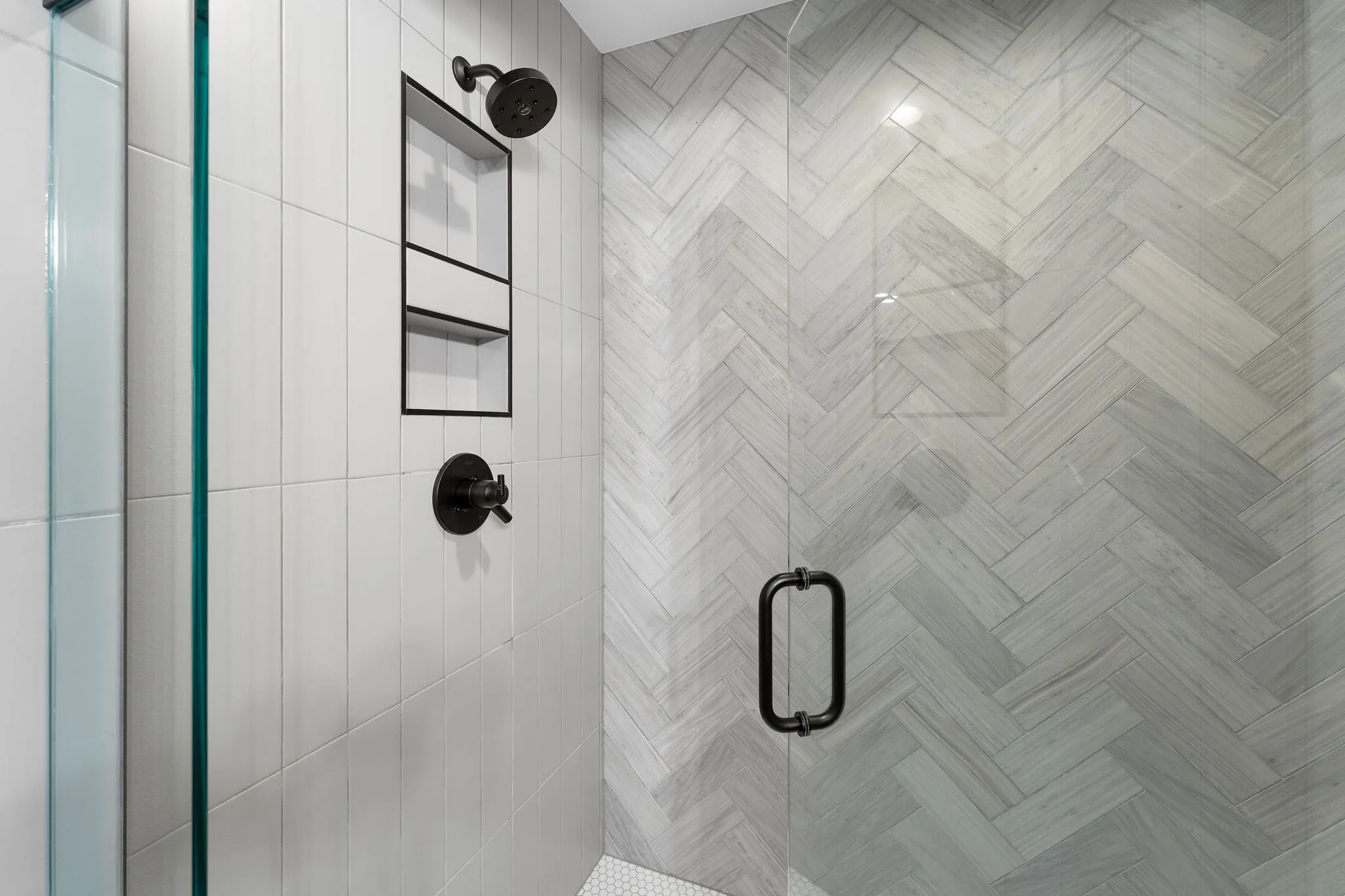 Light gray marble-patterned tiles in a chevron pattern next to vertical white subway tiles in a shower surroun