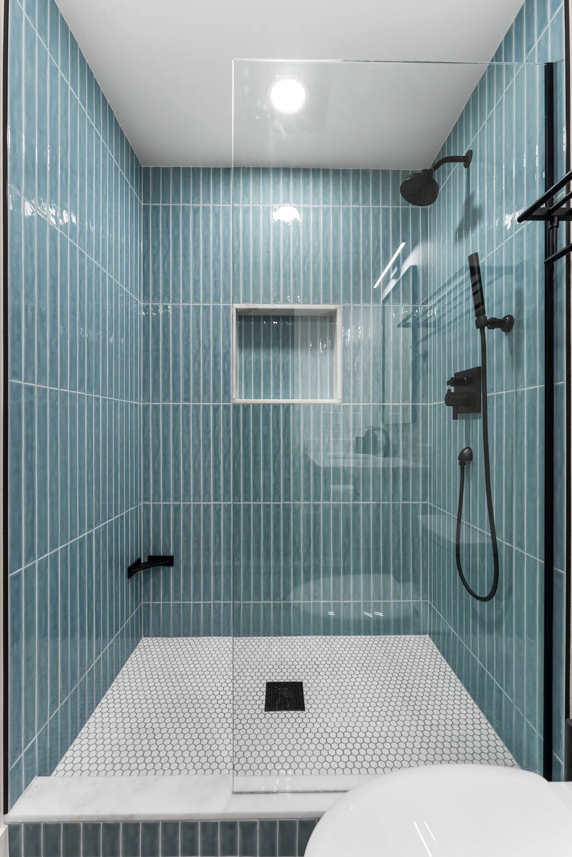 Vertically stacked blue kit-kat tiles on shower walls with a white penny tile floor.