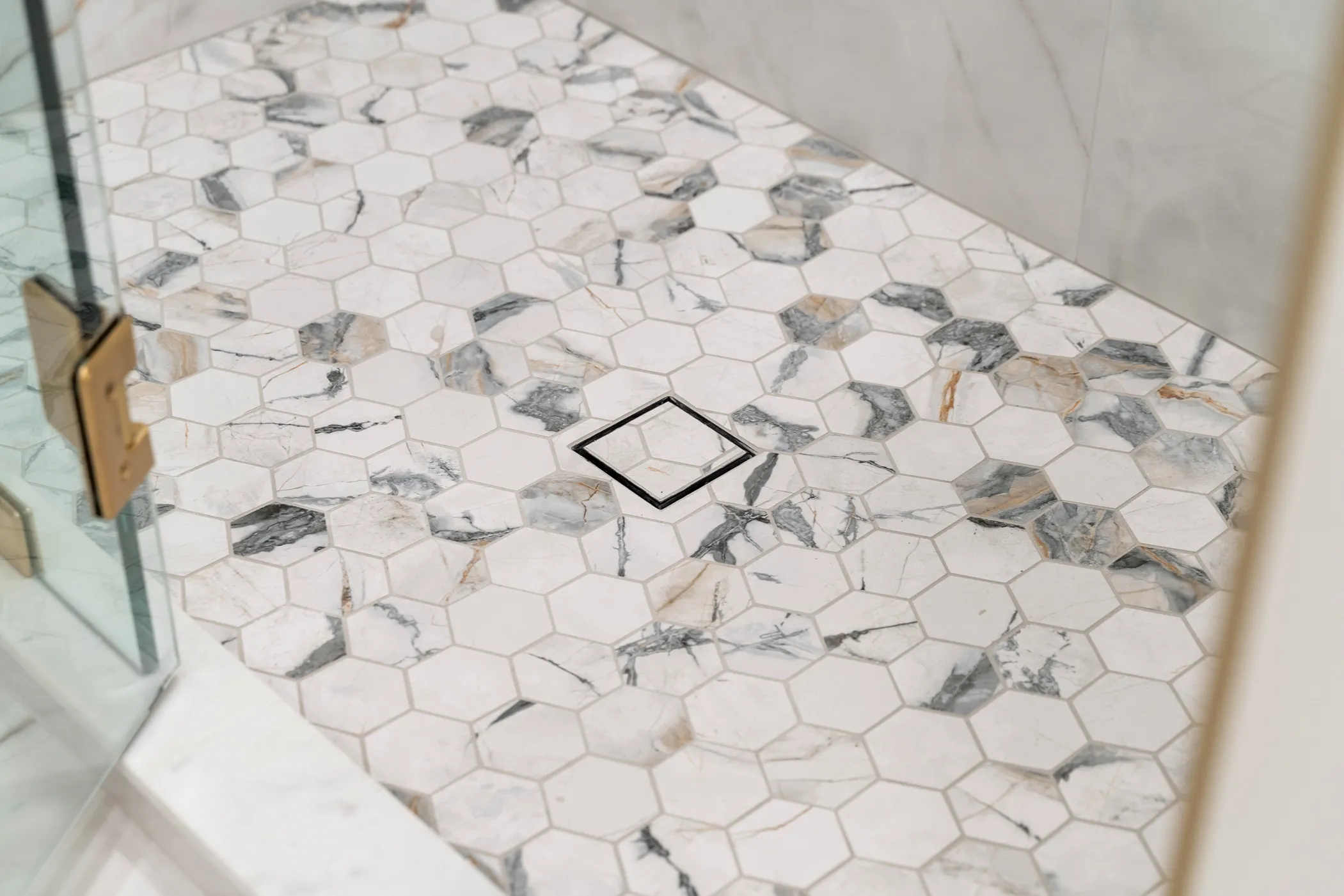 White marble-look hexagonal mosaic tiles on a shower pan floor with a black square drain.