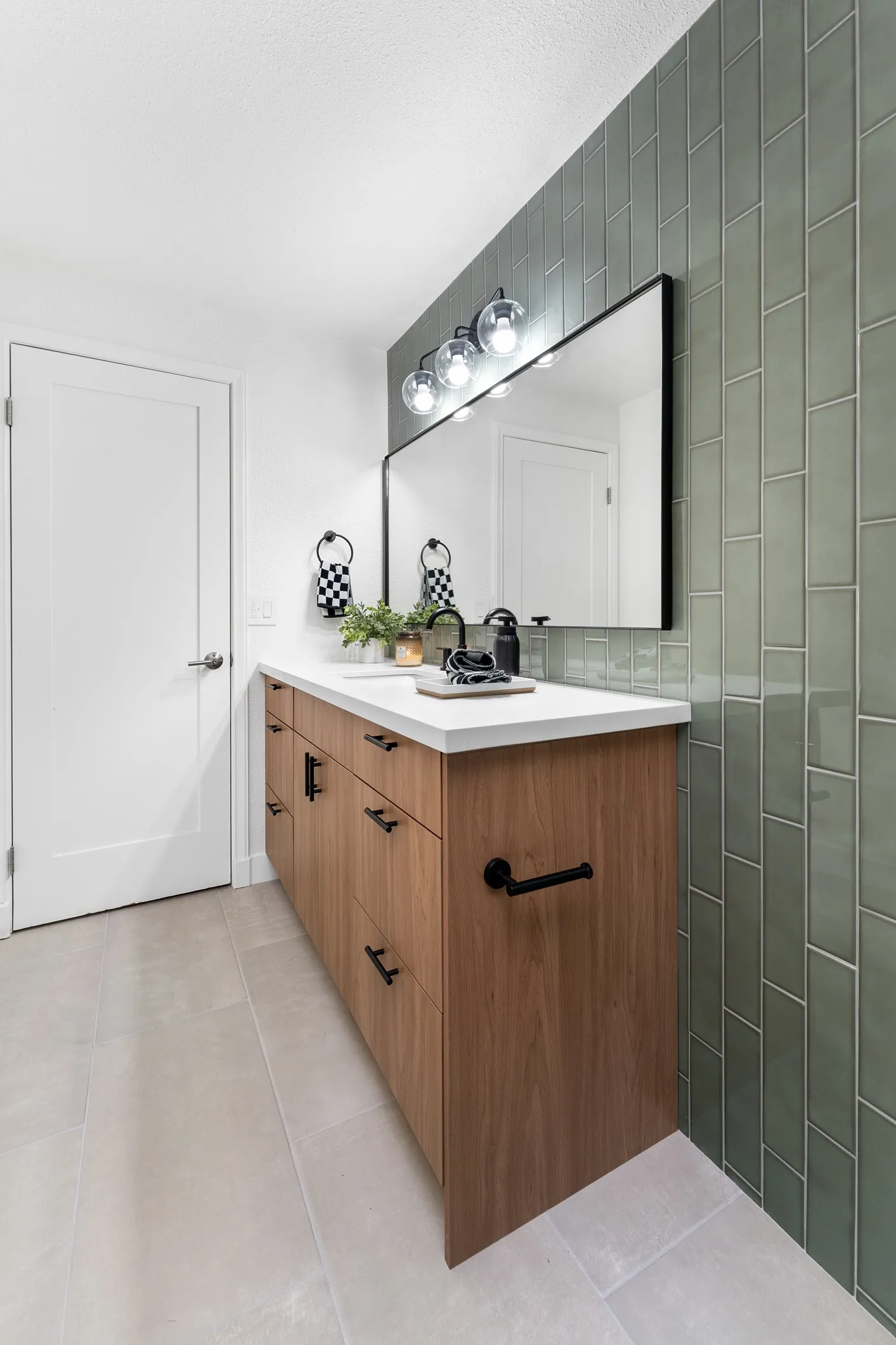 Sage green vertical subway tile feature wall installed behind a wood vanity and vanity mirror.