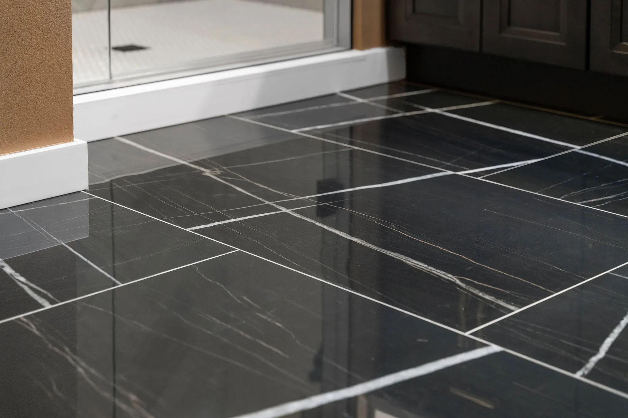 High-gloss black marble-look floor tiles with striking white veining installed near a white shower base.