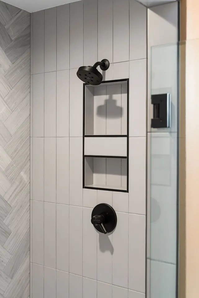 Vertical white subway tiles paired with a gray chevron marble-pattern tile accent wall in a shower.