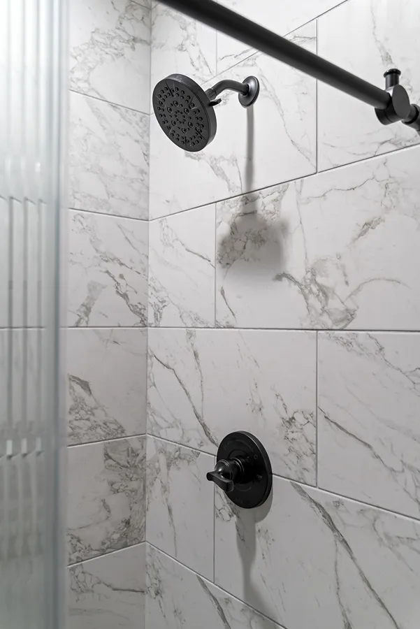 Large-format white marble-veined wall tiles installed horizontally in a shower surround.