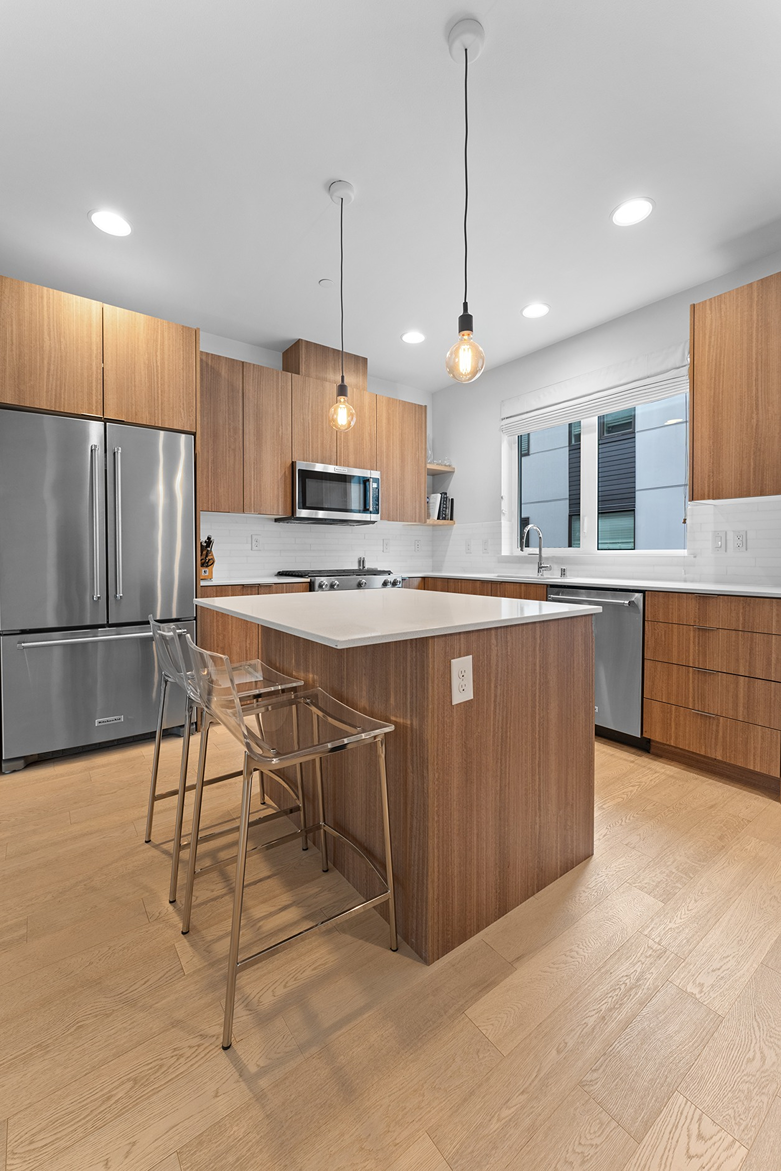 Modern kitchen island with white quartz countertops, warm wood-grain cabinets, and clear acrylic counter stools