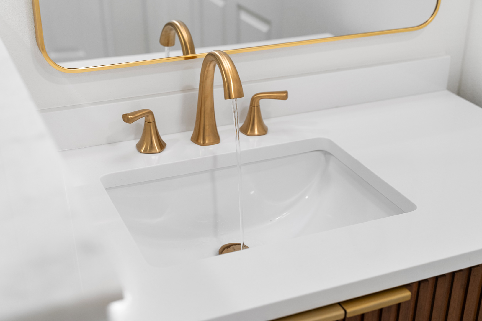 Polished white solid-surface vanity top featuring an under-mount basin with running water from a brushed brass gooseneck faucet.