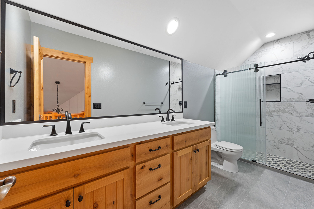 Long white double vanity countertop with dual under-mount sinks and matte black faucets mounted on natural wood cabinetry.