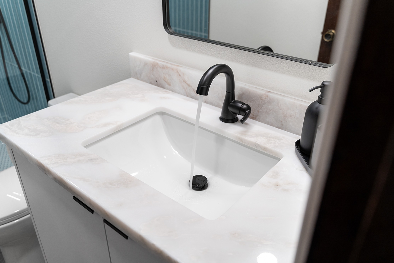 Single vanity top in white marble-patterned quartz with a short backsplash, under-mount sink, and matte black fixture.