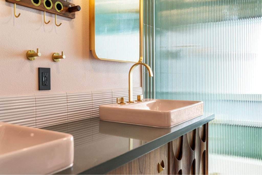 Polished dark gray quartz vanity top with vessel sinks and brushed gold faucets on a mid-century wood vanity