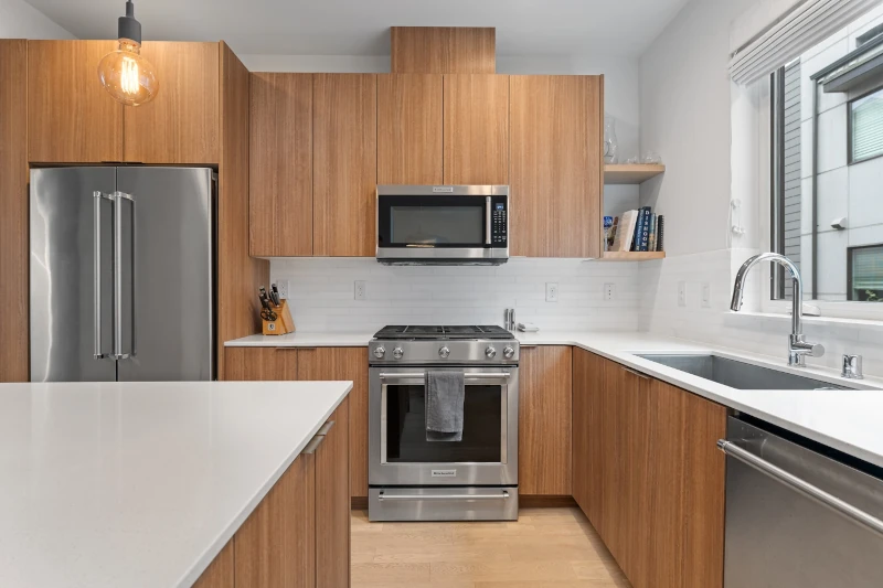 Modern kitchen with light wood flat-panel cabinets, stainless steel appliances, white quartz countertops, and minimalist design in a bright, natural light-filled space