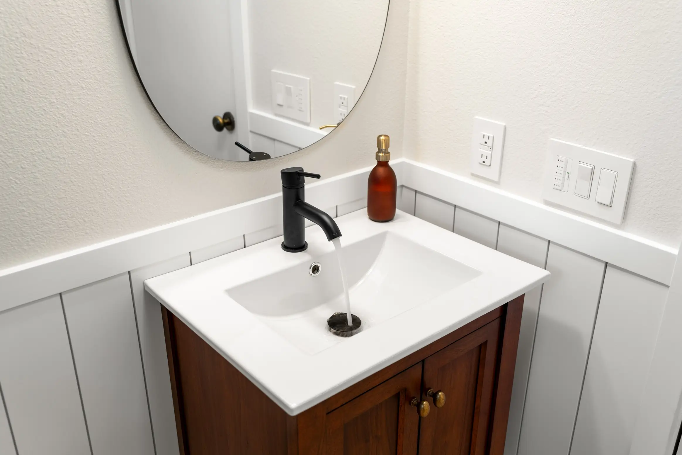 A vanity mirror with a simple white sink underneath and faucet left turned on