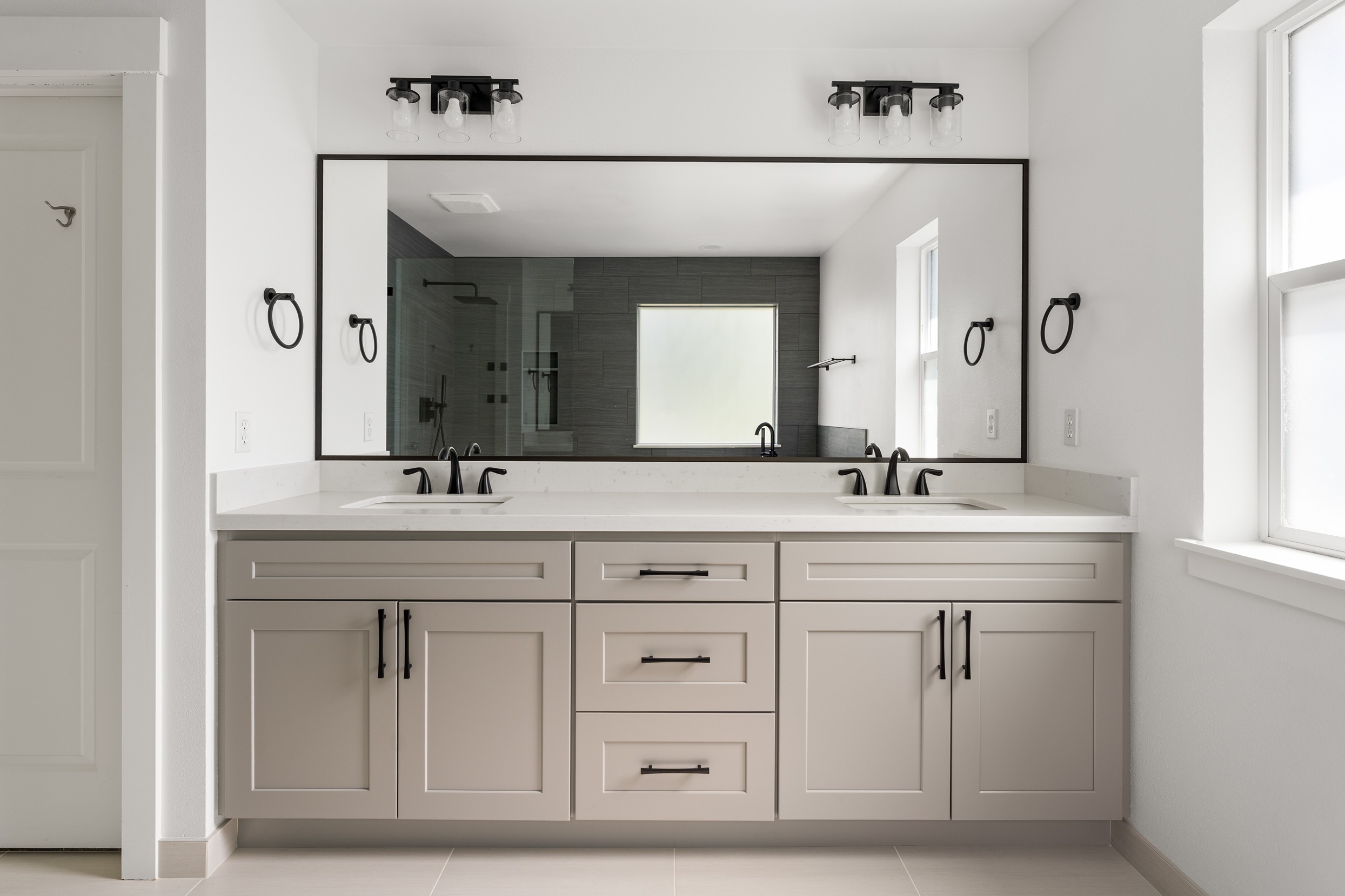 A large vanity mirror with two sinks underneath and cabinets for storage 