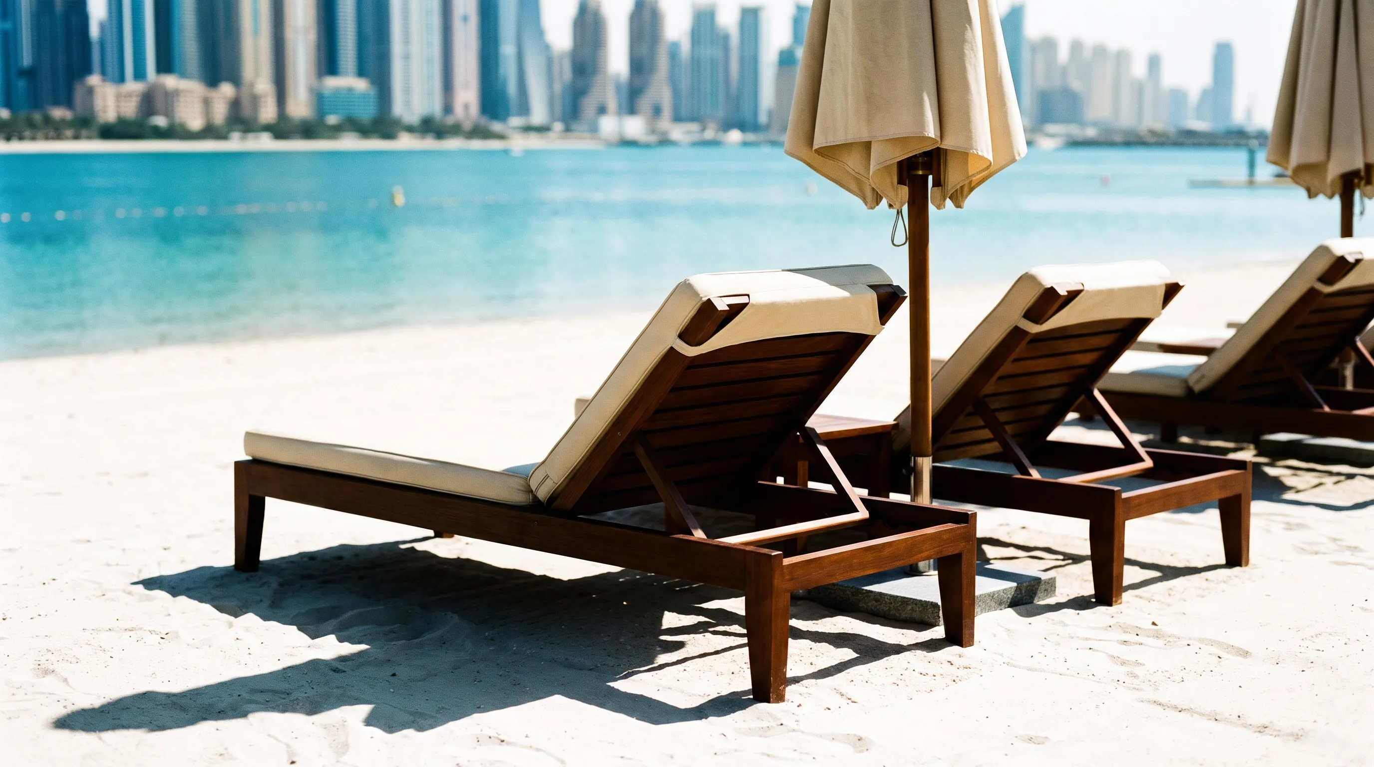 Ligbedden op het witte strand van een resort op Palm Jumeirah met de skyline van Dubai Marina