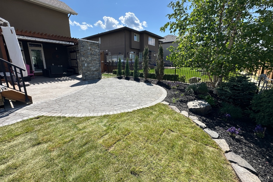 Backyard landscape construction in Calgary featuring a circular interlocking paver patio, stone column, and dark mulch beds by Western Elements Landscaping