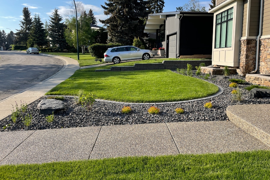 Front yard curb appeal with fresh sod and curved dark river rock garden beds, Calgary landscaping by Western Elements Landscaping