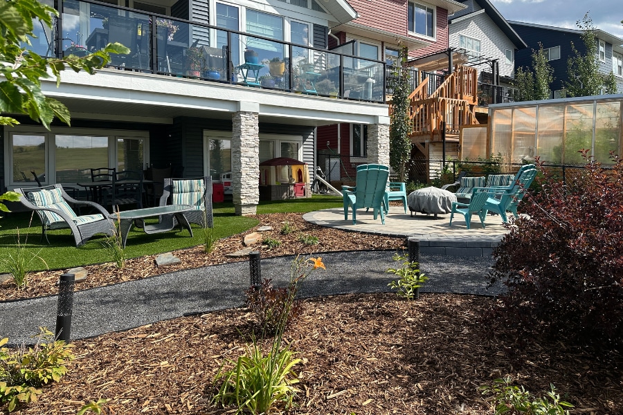 Backyard gravel patio with teal outdoor chairs, mulch garden beds, and a wood deck, a landscape in Calgary by Western Elements Landscaping