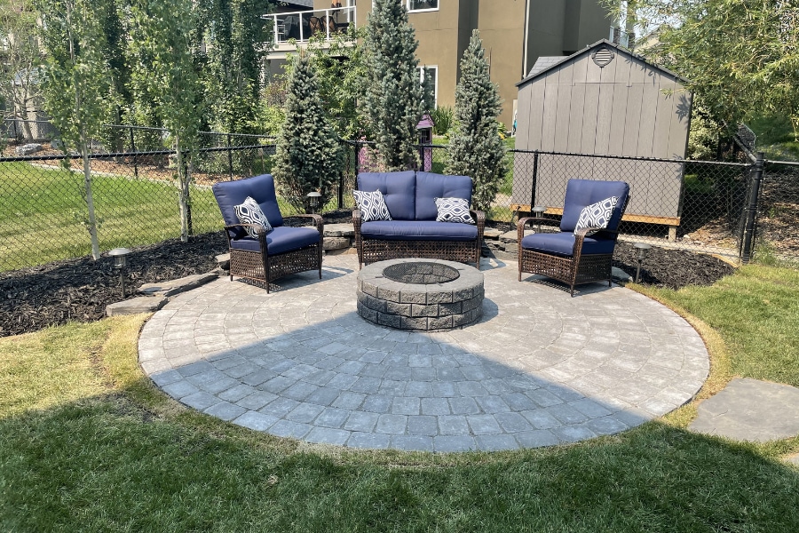 Circular interlocking paver fire pit patio with navy blue wicker furniture and dark mulch garden beds, Calgary landscaping by Western Elements Landscaping