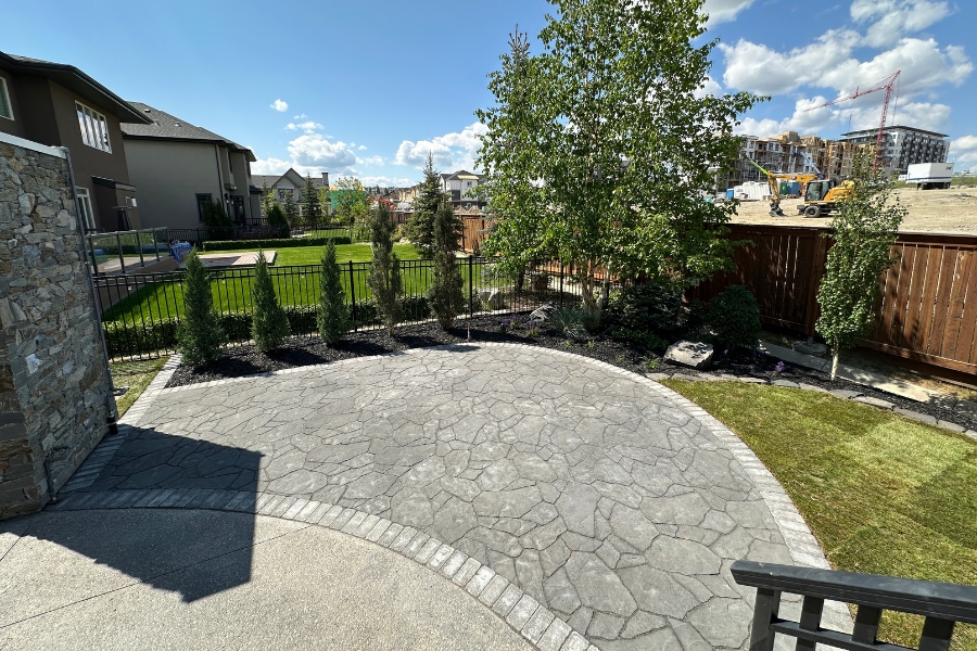 Large curved flagstone-pattern interlocking paver patio with dark mulch garden beds and iron fencing, a landscape design and build in Calgary