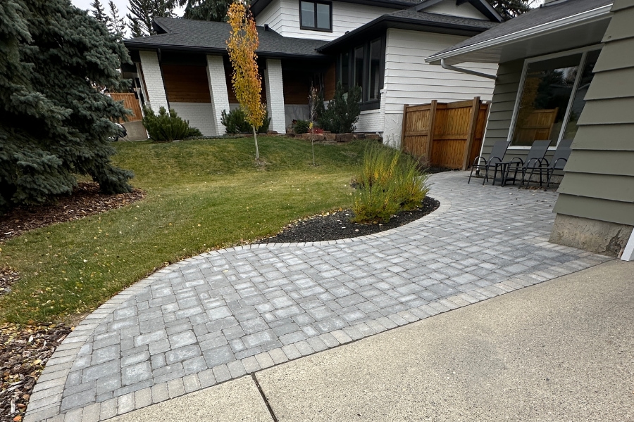 Curved interlocking paver front walkway with dark mulch garden beds and ornamental grasses, landscape construction in Calgary