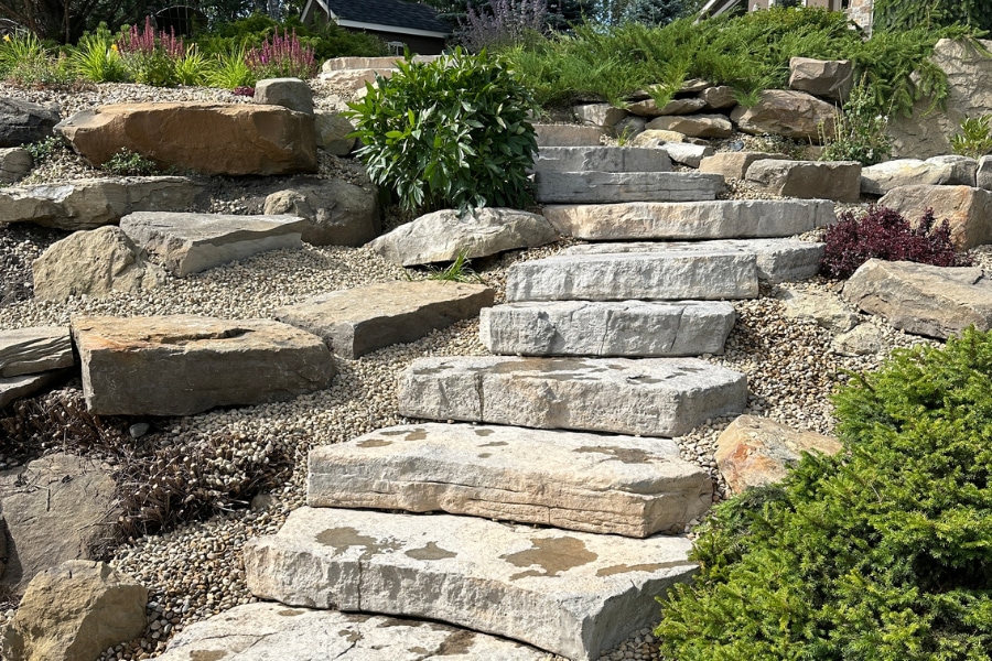 Natural flat stone steps with large boulder accents and river rock garden beds by a landscape design contractor in Calgary